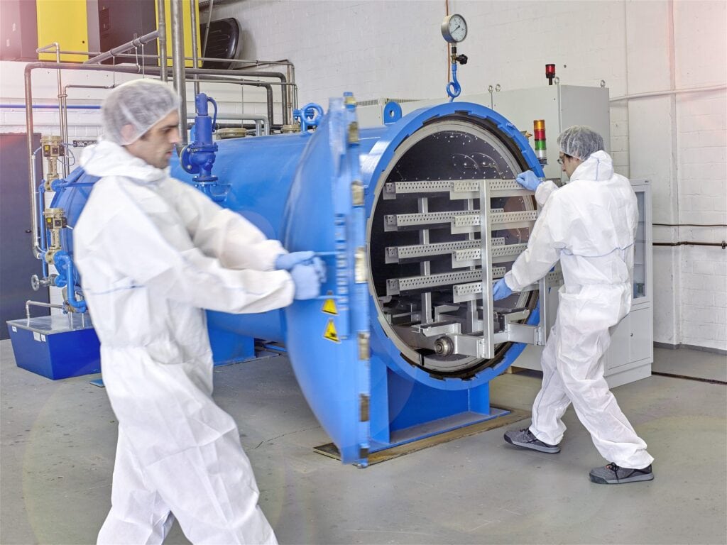 Zwei Mitarbeiter in Schutzkleidung an einem geöffneten Autoklav bei MBM Techglas